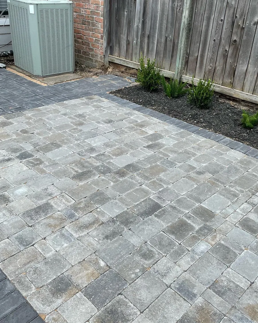 Gray paver patio with a fresh planting bed along a wood fence