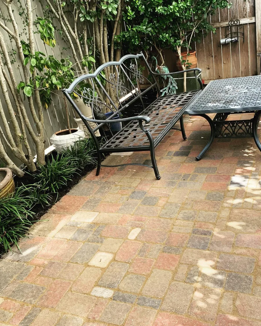 Brick paver patio with a bench and table tucked against a planted fence line